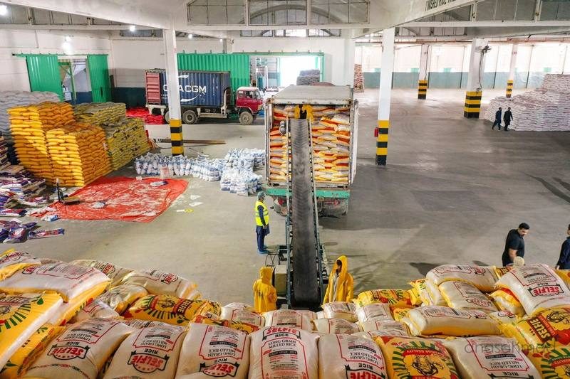 Elevated view of a rice packaging warehouse with stacked sacks and workers on the floor
