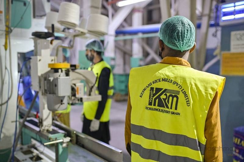 Factory worker in hairnet and safety vest observing rice packaging machinery