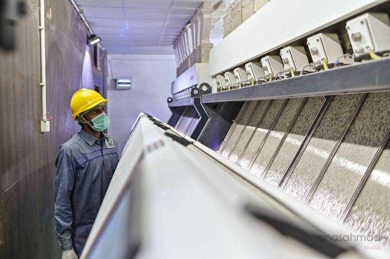 Factory worker in hard hat and mask monitoring industrial textile machinery