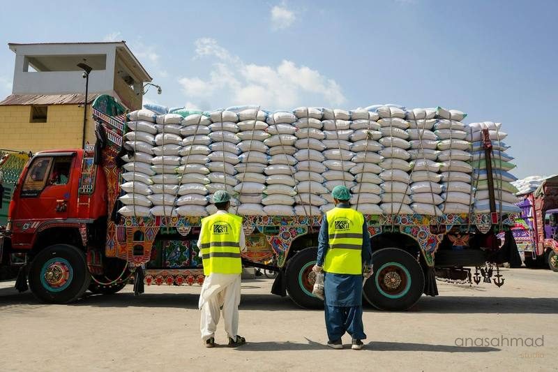 Two workers in high-visibility vests inspecting a fully loaded rice mill delivery truck