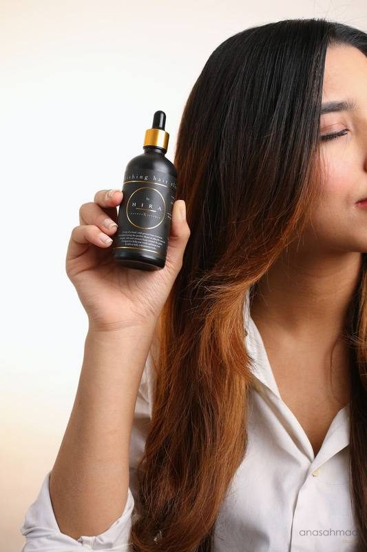 HIRA nourishing hair elixir bottle held next to model's hair