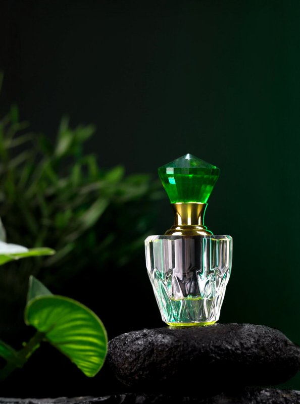 Emerald-cut perfume bottle with gold neck, styled on dark stone with greenery
