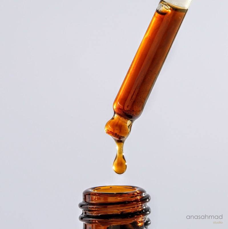 Amber serum dropper bottle with suspended droplet, macro shot on white background