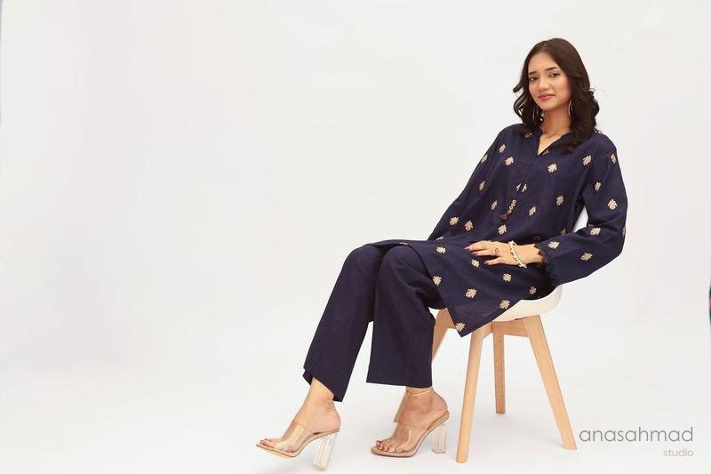 Model in navy embroidered kurta suit, seated portrait on white background
