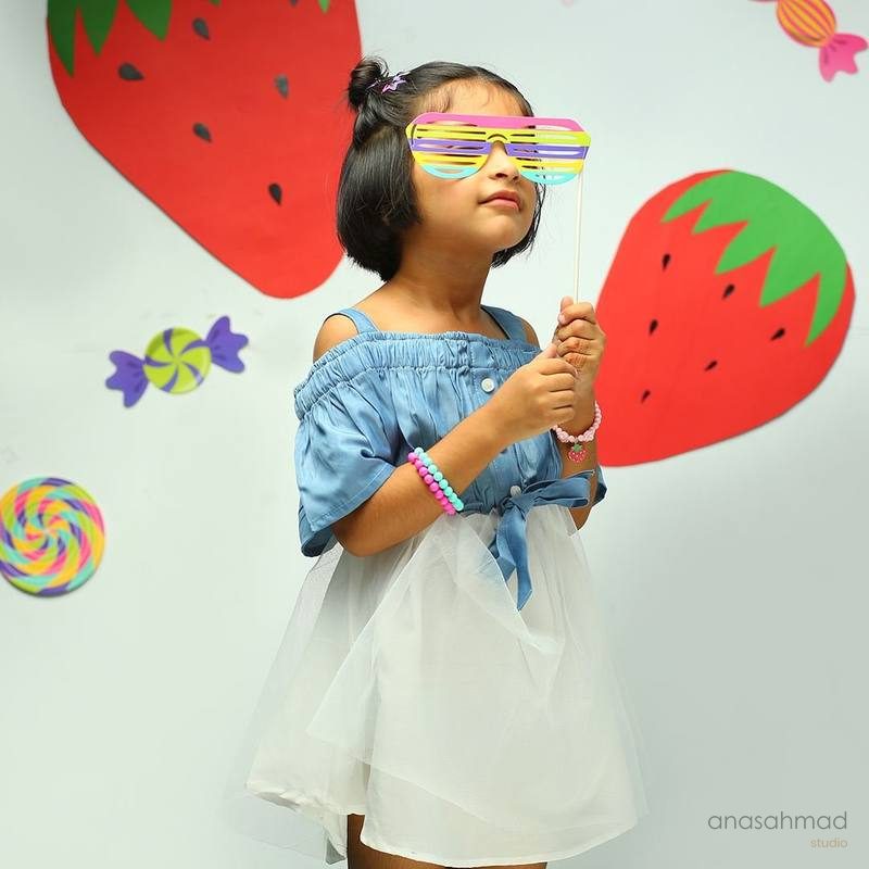 Child model in denim and tulle outfit with playful strawberry and candy backdrop
