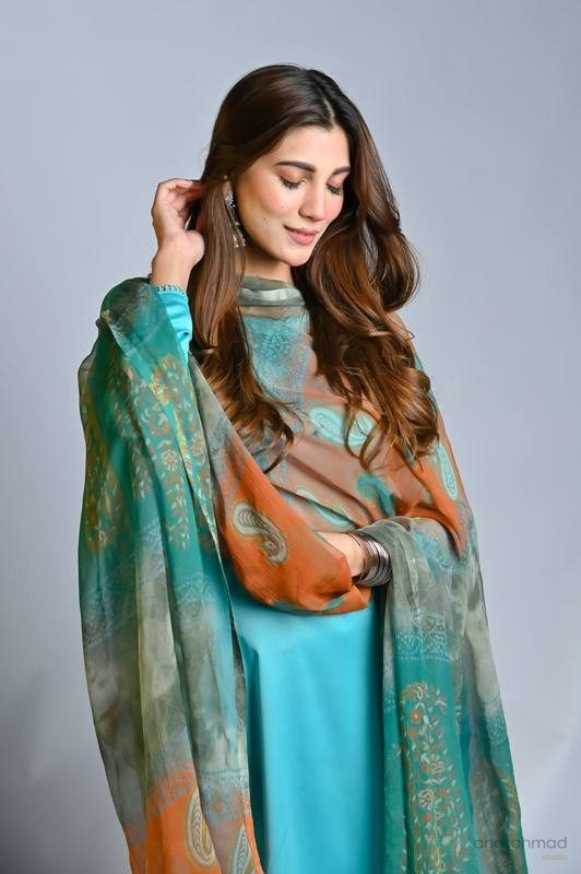 Model in turquoise silk suit with orange and teal printed paisley dupatta, candid pose