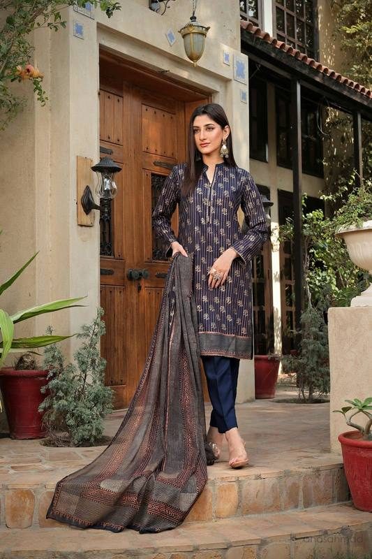 Model in navy blue printed kurta suit with striped dupatta, standing in front of a carved wooden doorway