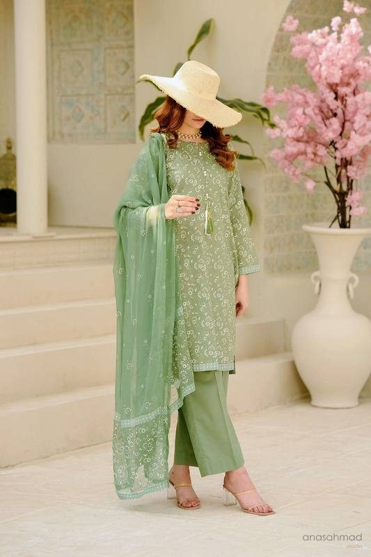 Model in sage green embroidered kurta suit with straw sun hat, styled with pink blossom branches
