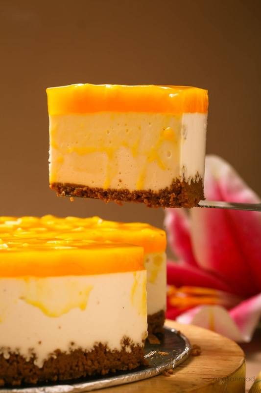 Mango cheesecake slice with glossy mango glaze being lifted from the whole cake — Anas Ahmad Studio, Karachi