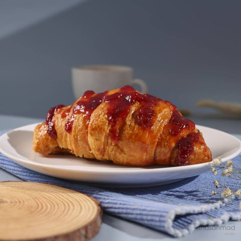 Croissant topped with strawberry jam on a white plate