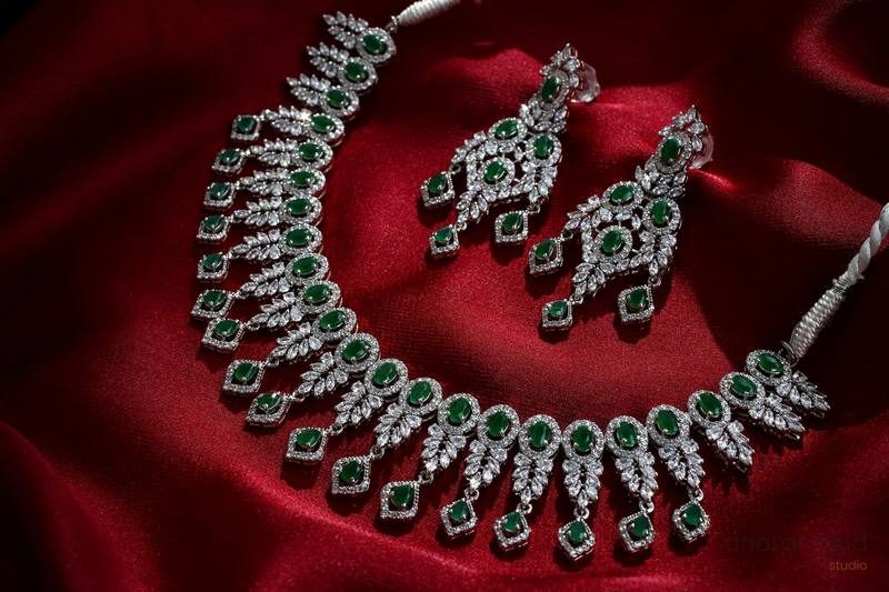 Emerald and diamond necklace and earring set on red satin fabric — Anas Ahmad Studio, Karachi