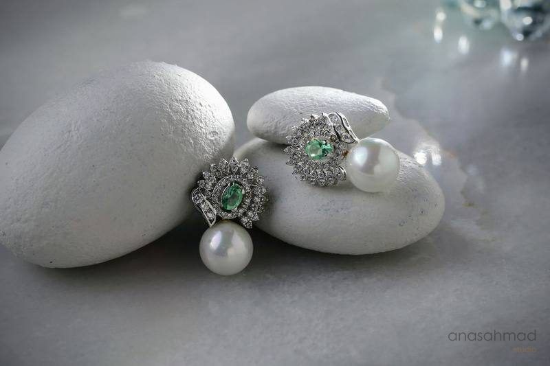 Emerald and pearl drop earrings displayed on white stones
