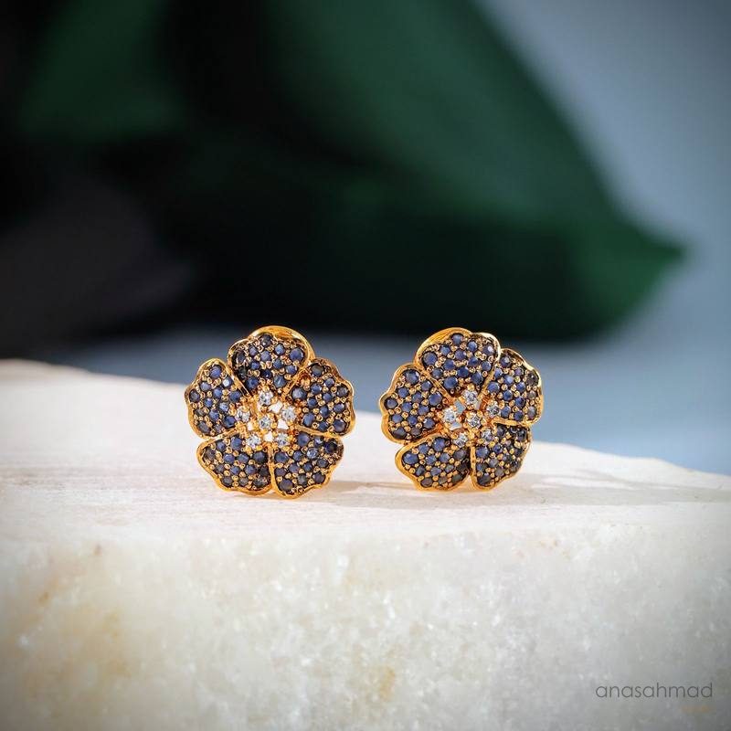 Sapphire flower-shaped stud earrings on marble with green leaf background