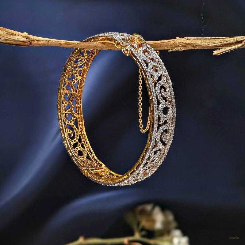 Gold and diamond filigree bangle bracelet hanging from a branch