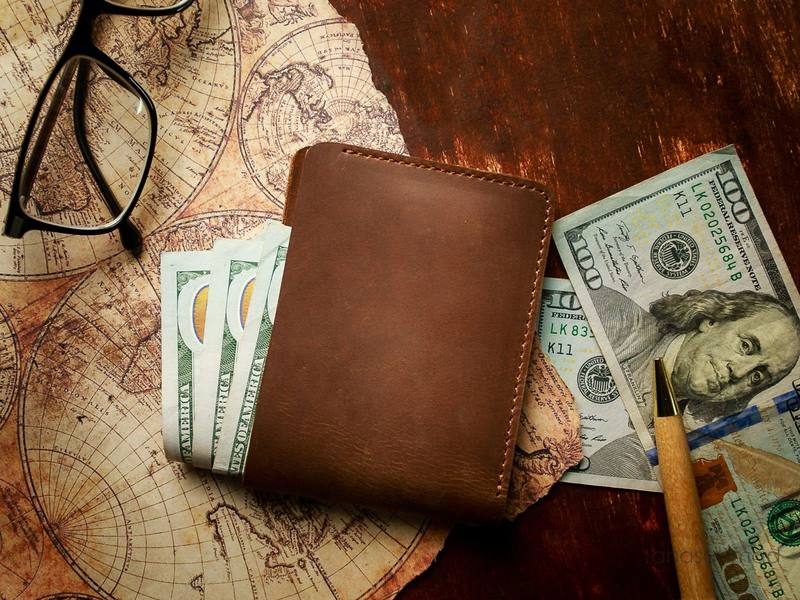 Brown leather wallet with cash, glasses and pen, styled on a vintage map