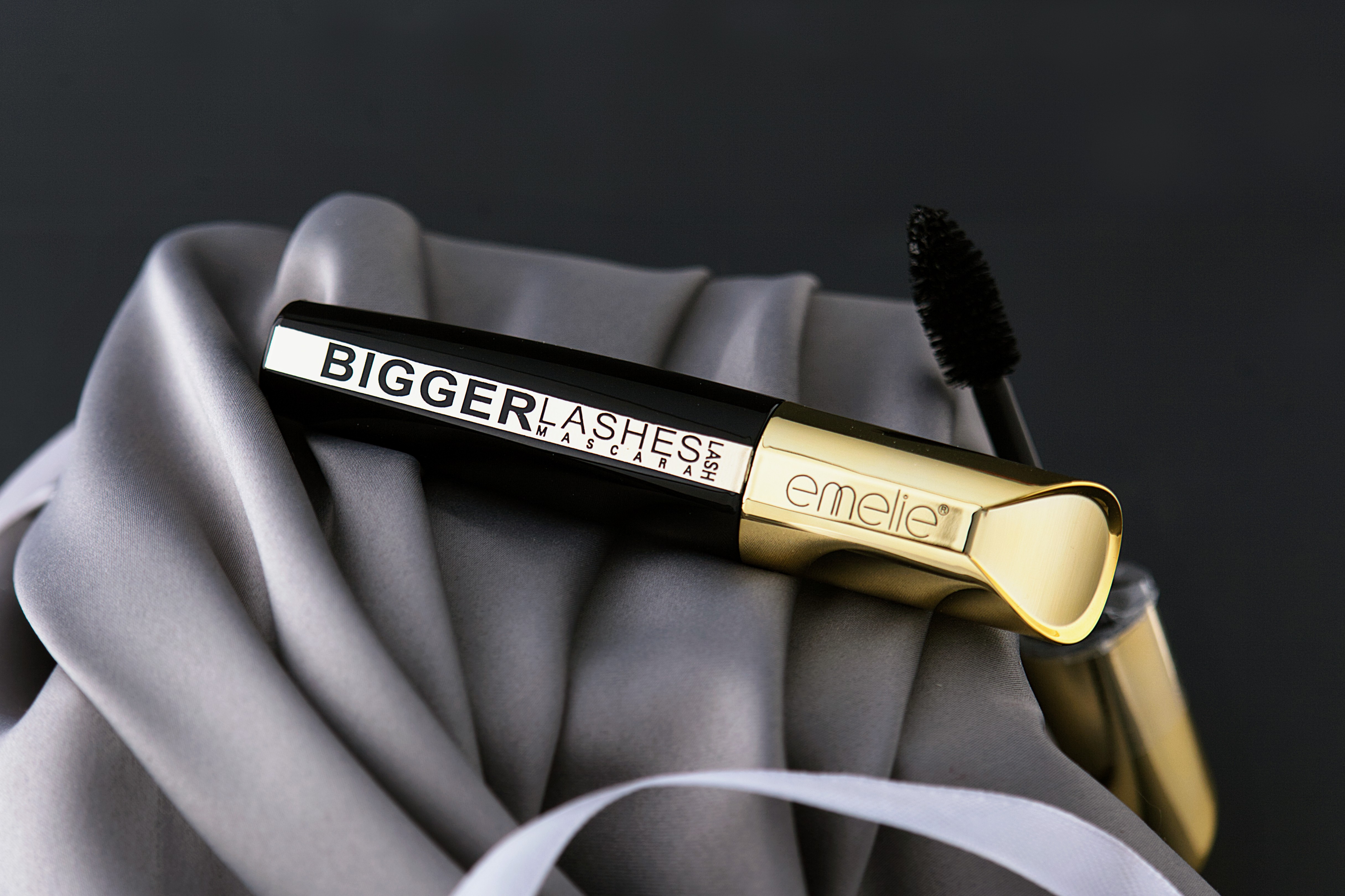 Black mascara tube with applicator brush on soft fabric background